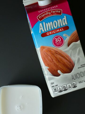 carton of almond milk on black background with small square container of milk ready to freeze.