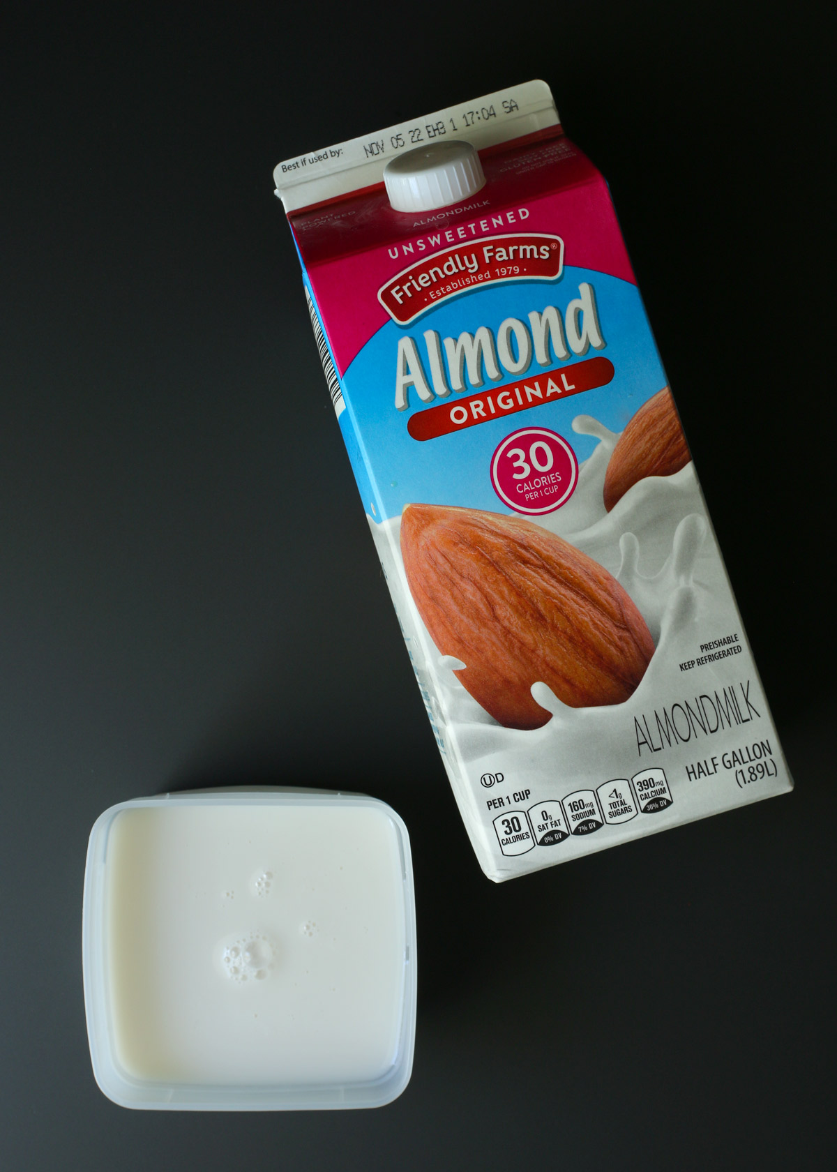 carton of almond milk lying on a black surface with a small container of milk nearby.