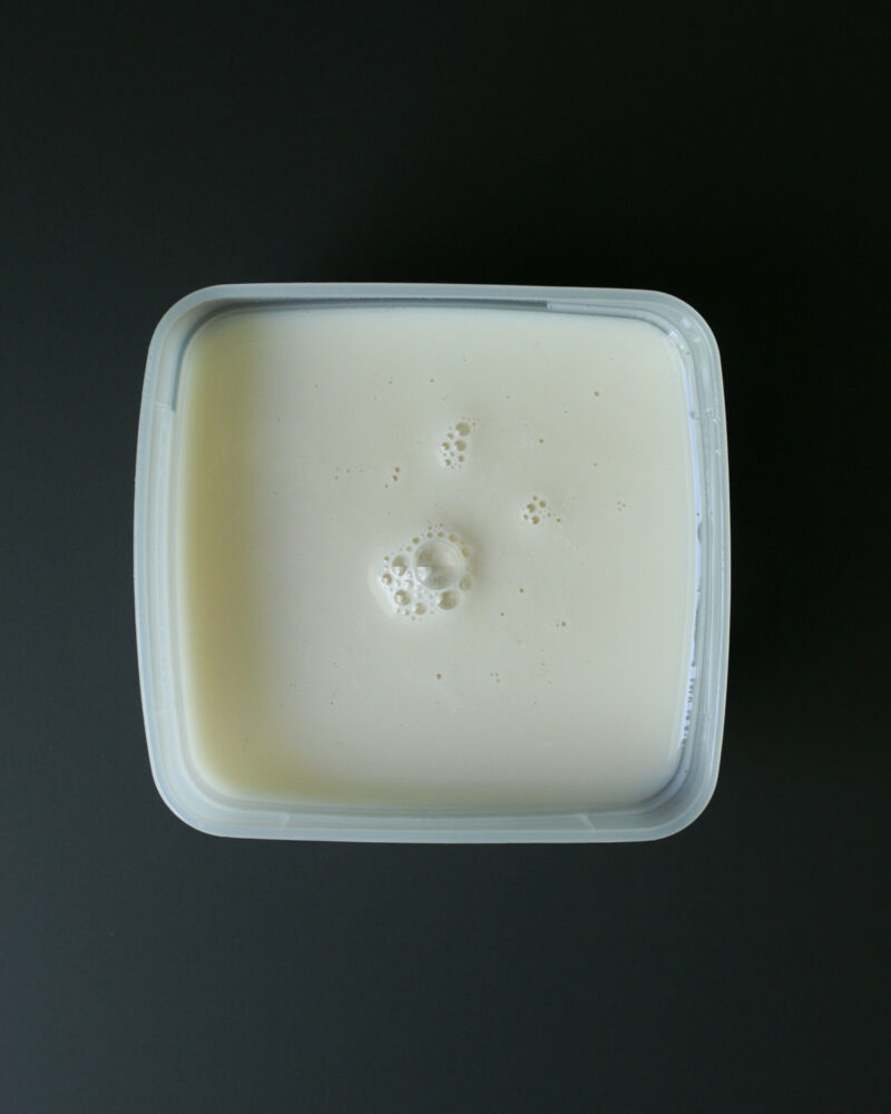 almond milk in a small plastic container on a black table.