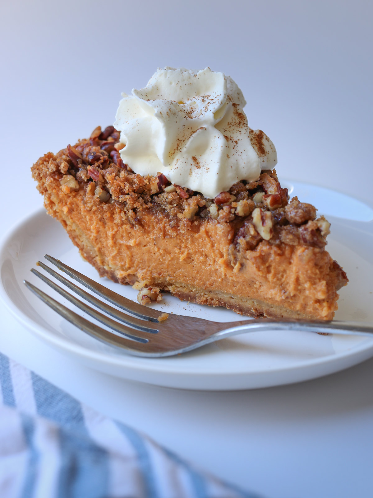 slice of pumpkin pie with a graham cracker crust on a plate with a fork nearby.