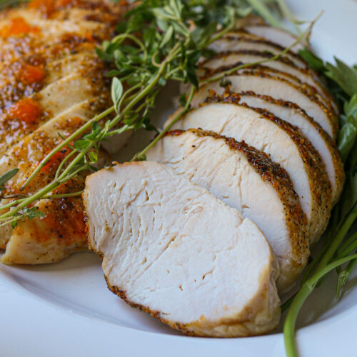 sliced air fryer turkey tenderloin on platter with fresh herbs.