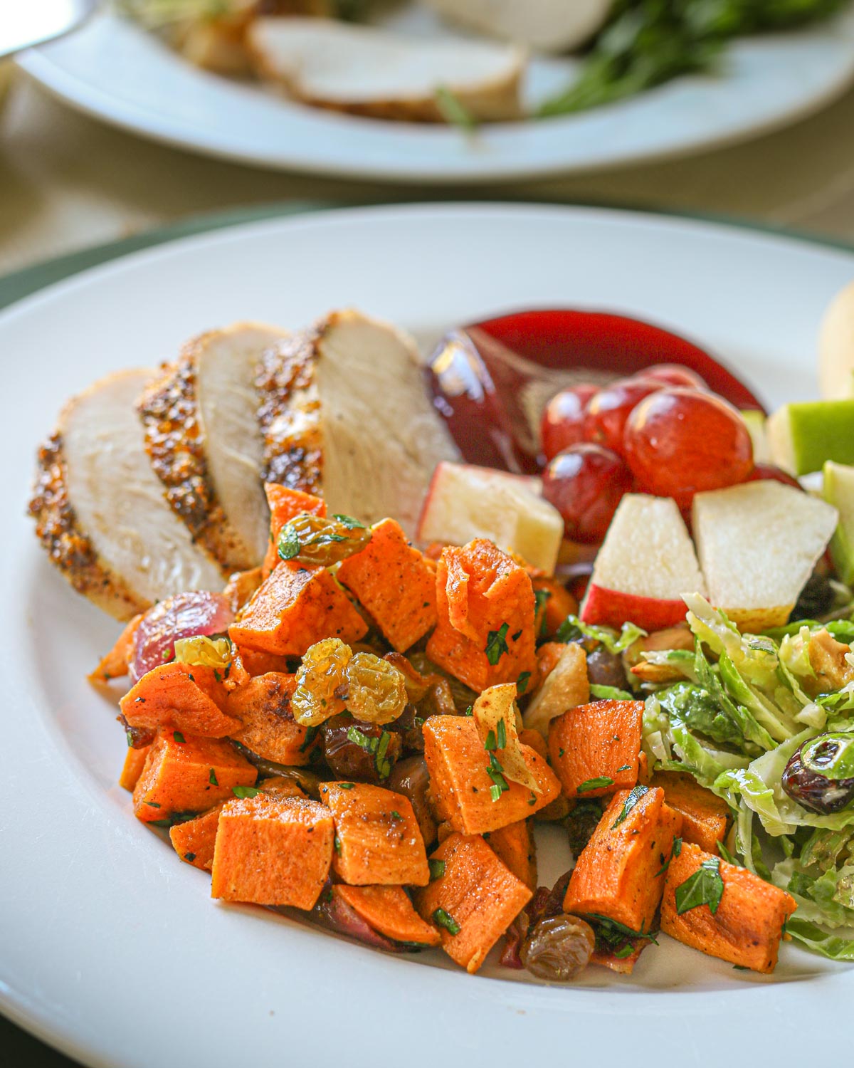 close up of sweet potato salad on dinner plate with turkey, cranberry sauce, and other sides.