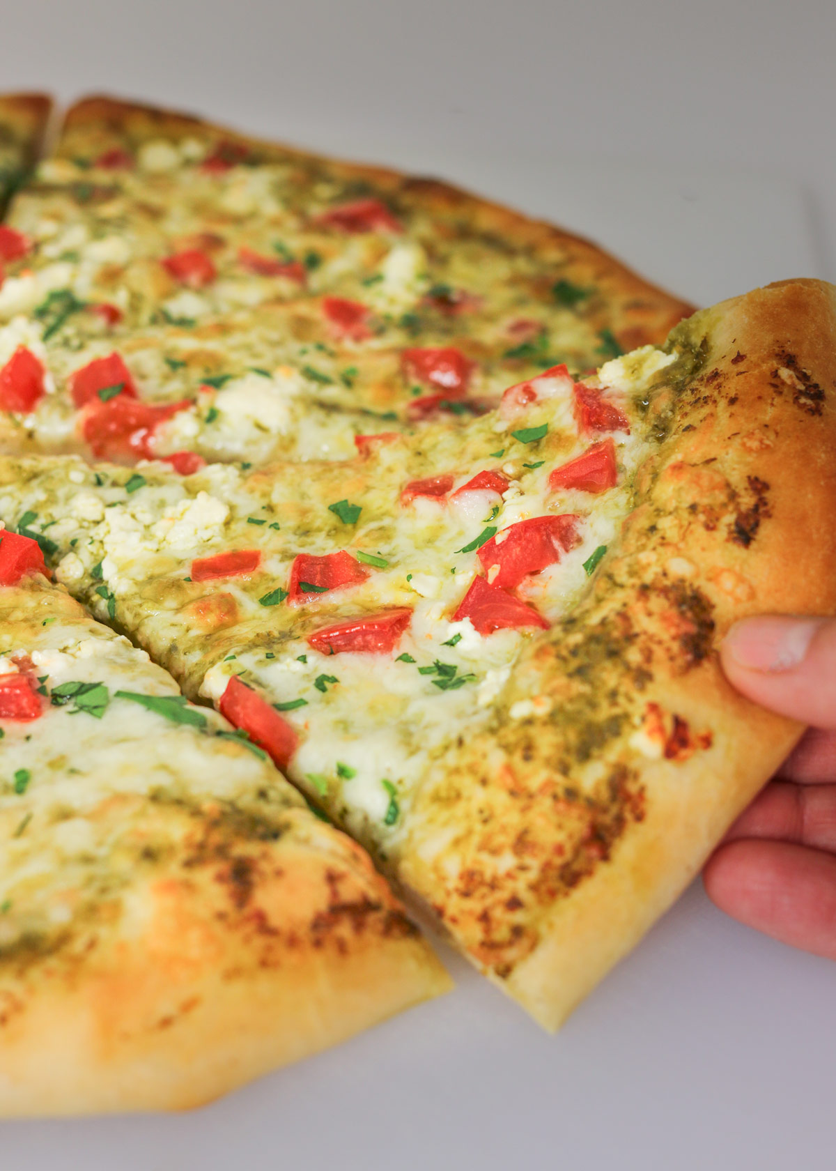 hand reaching for the slice of pesto pizza from a whole pizza.
