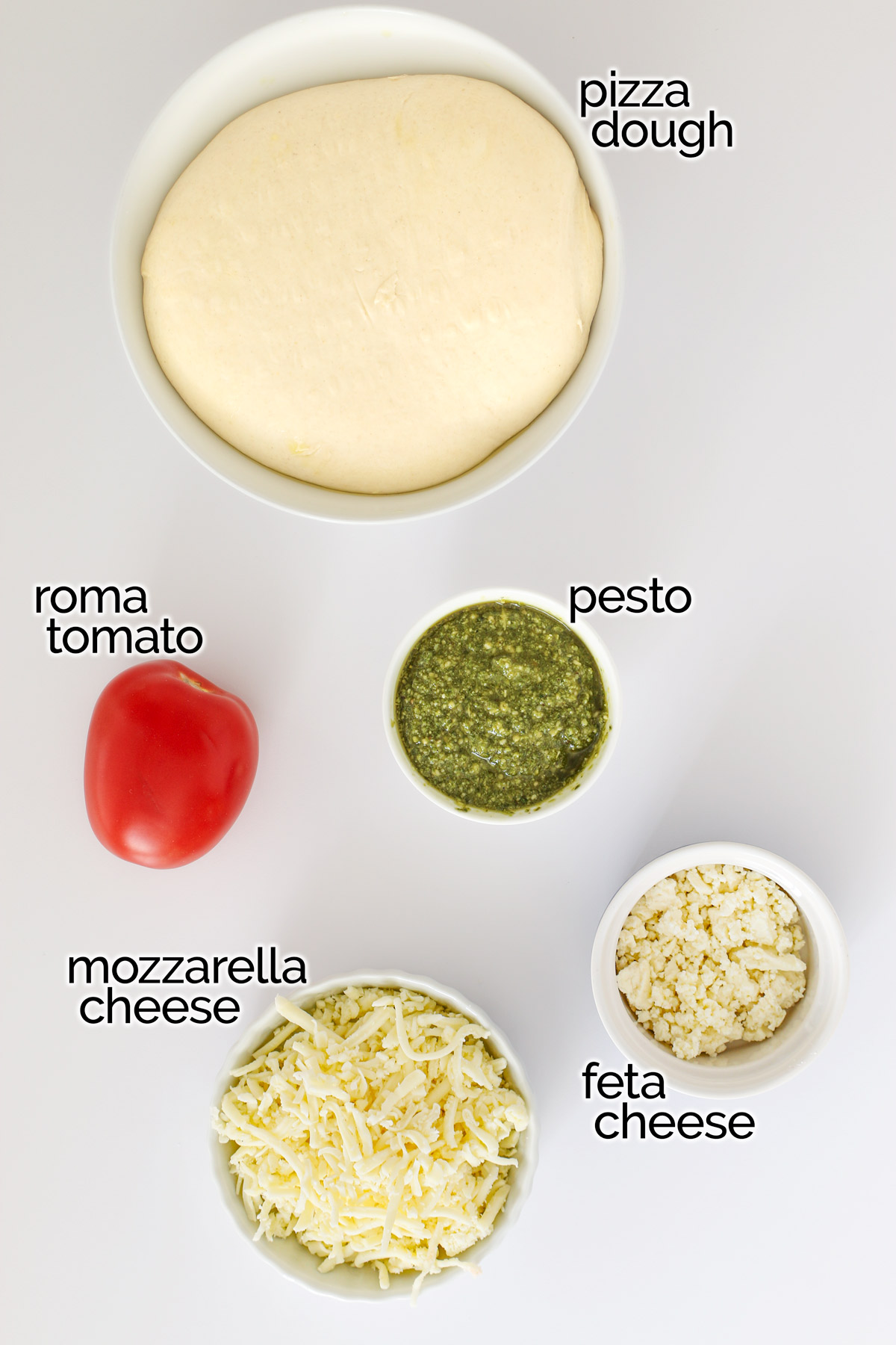 ingredients for pesto pizza laid out on the white counter.