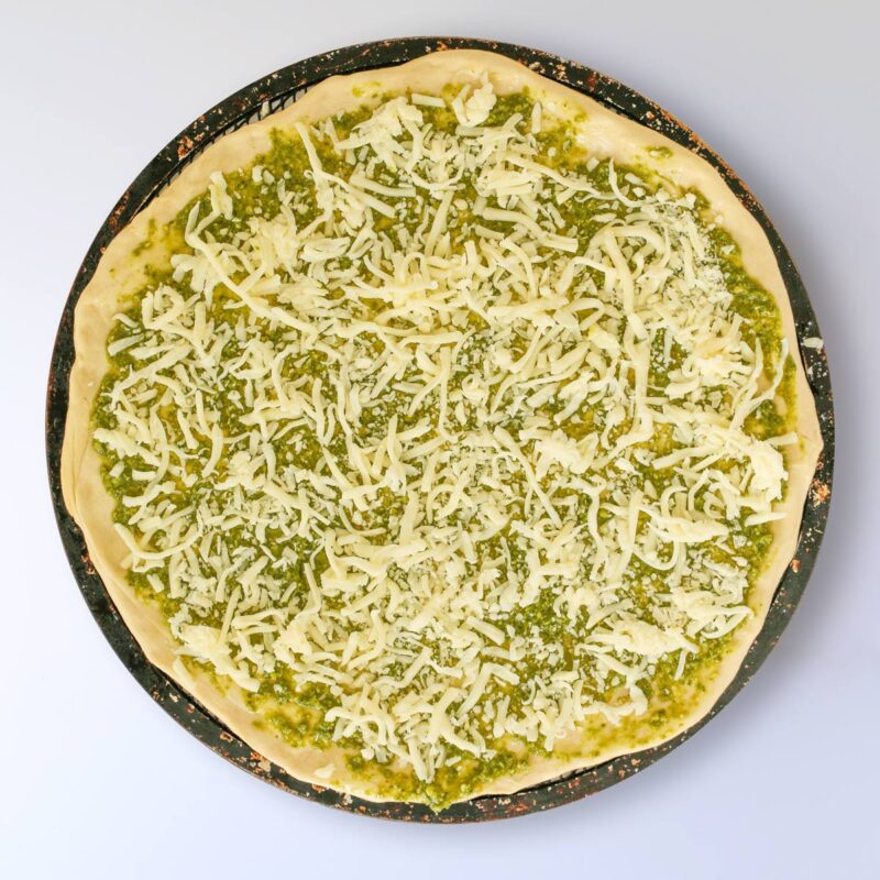 cheeses sprinkled across the pesto on the pizza dough.
