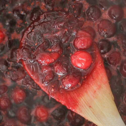 close-up shot of cooked cranberry sauce on wooden spoon.