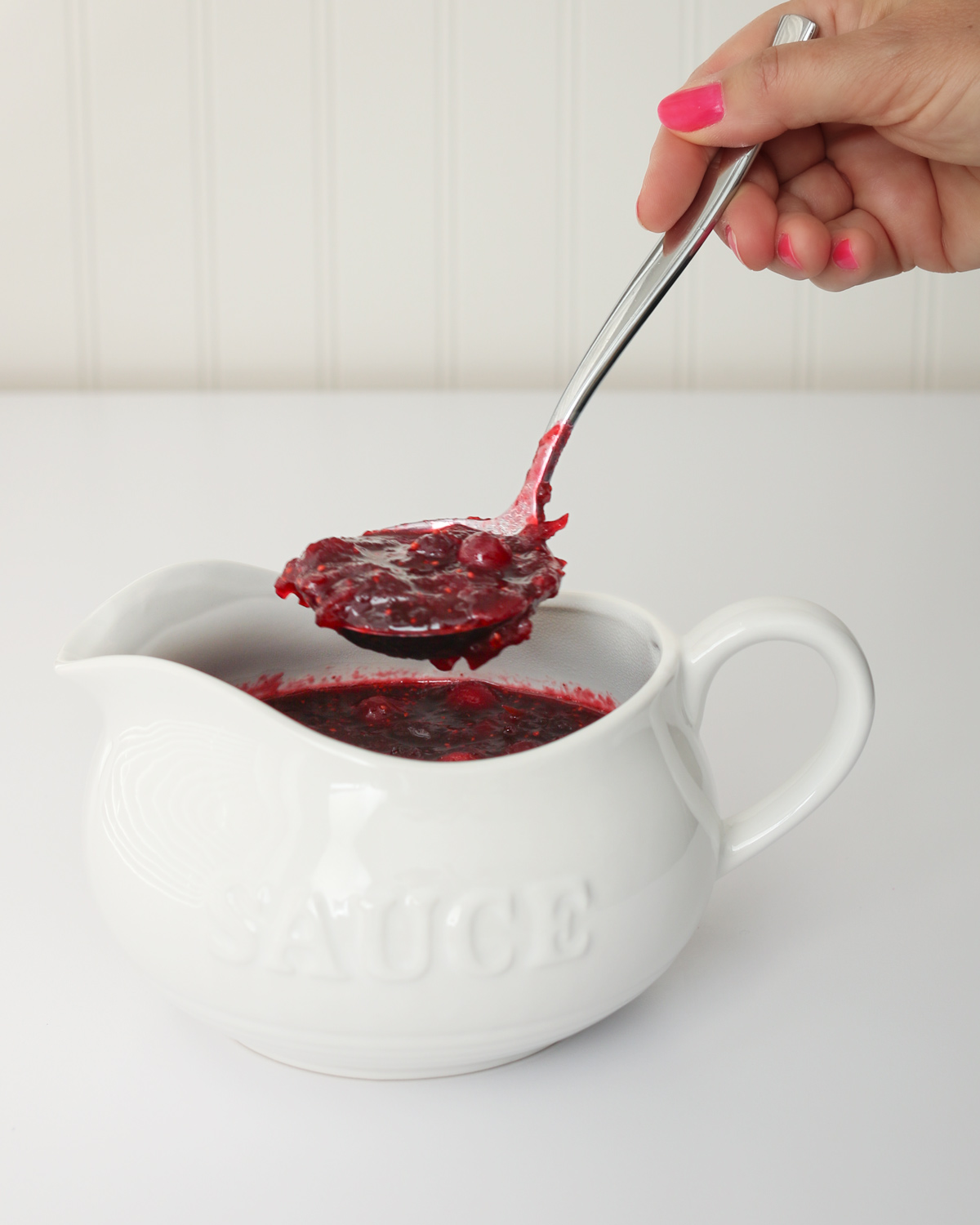 ladling cranberry sauce from a white sauce boat.