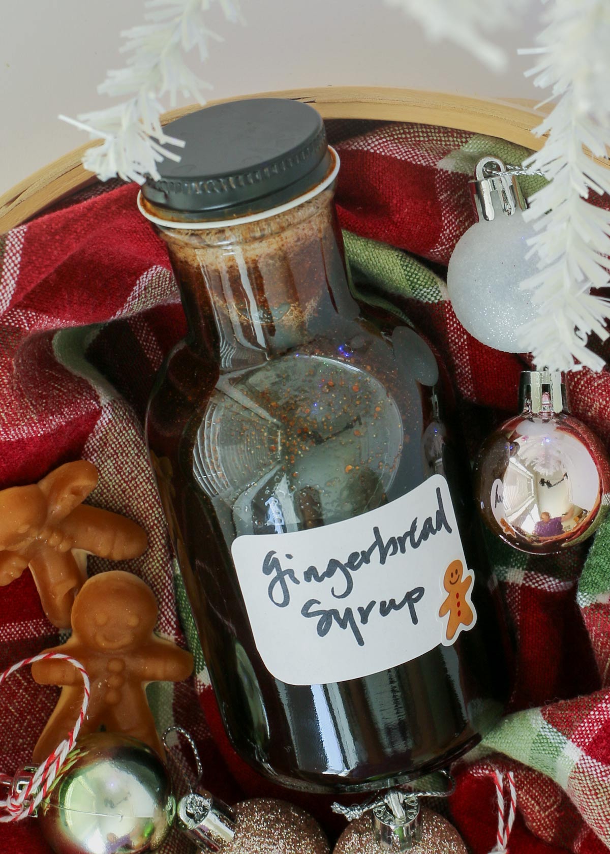 bottle of gingerbread syrup in a basket with ornaments and candies.