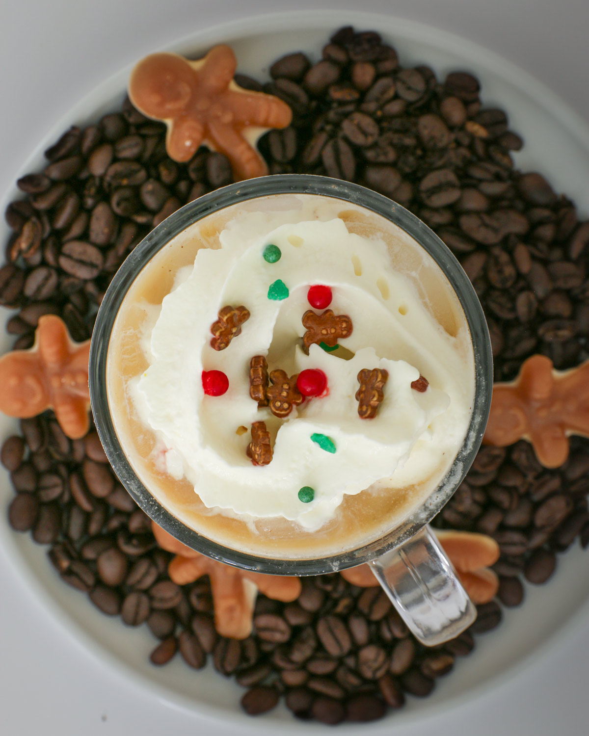 gingerbread latte in glass mug surrounded by coffee beans and gingerbread men candies.