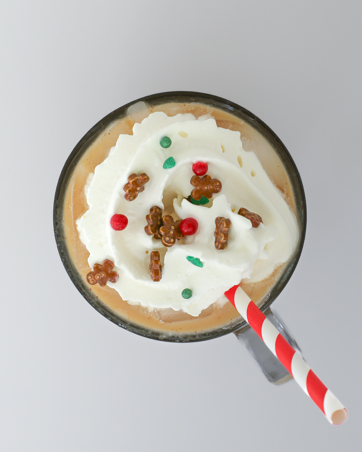iced gingerbread latte with whipped cream and gingerbread sprinkles and a red striped straw.