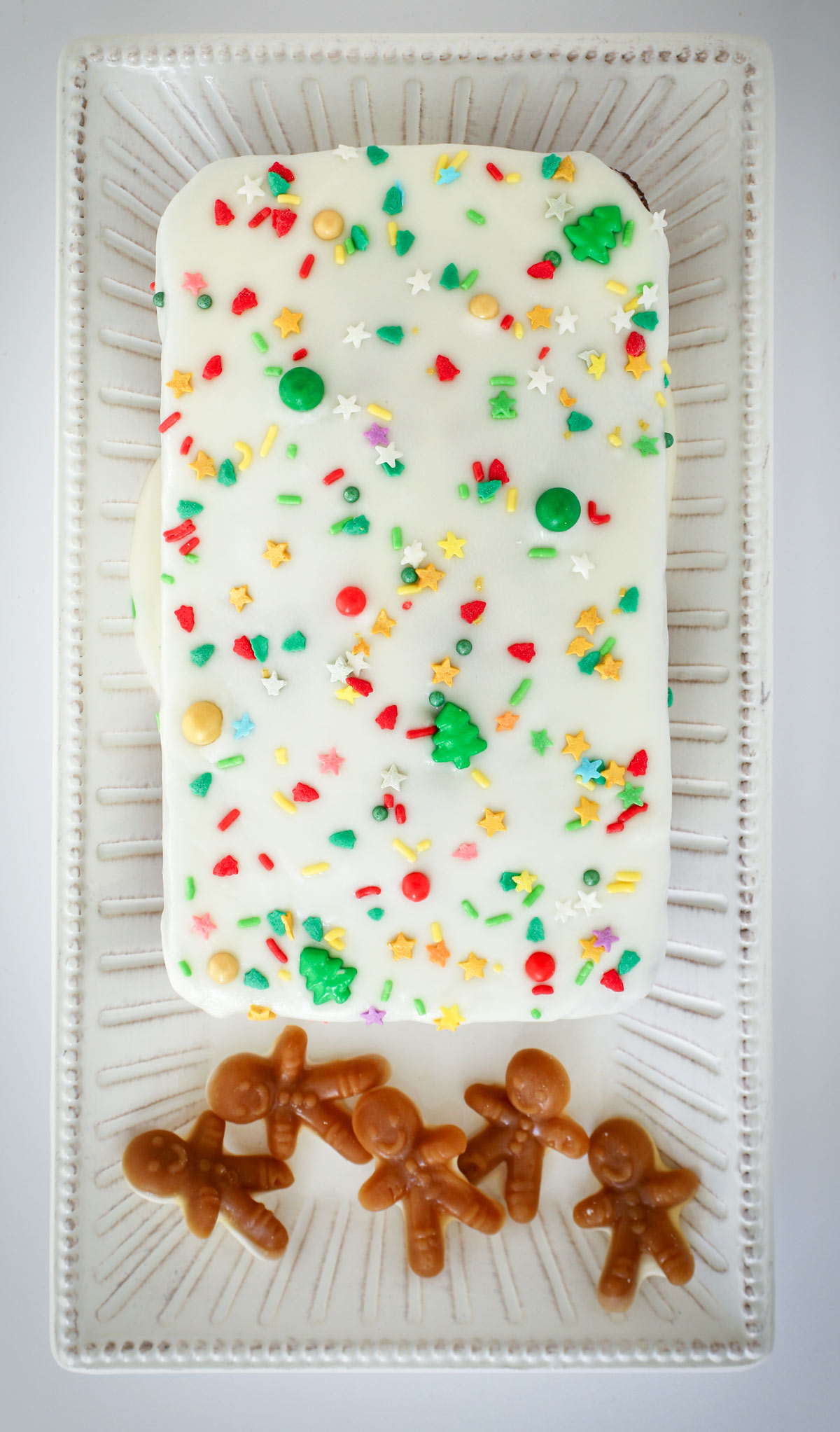 glazed gingerbread loaf cake topped with Christmas sprinkles, a few gingerbread man candies sitting on the end of the platter.