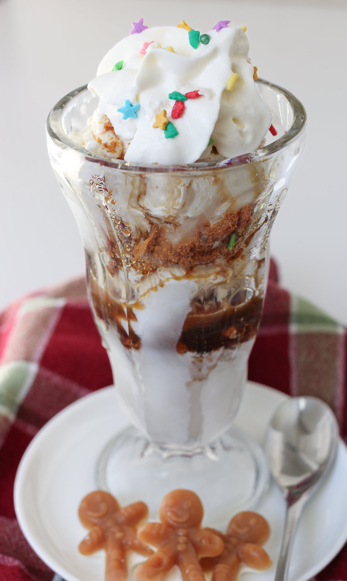 gingerbread ice cream sundae in a tall sundae glass with a spoon and gingerbread men candies on the saucer.