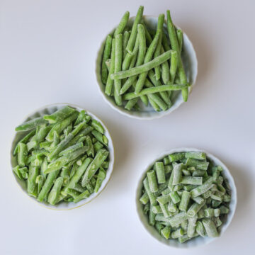 bowls of different cuts of frozen green beans on a white counter.