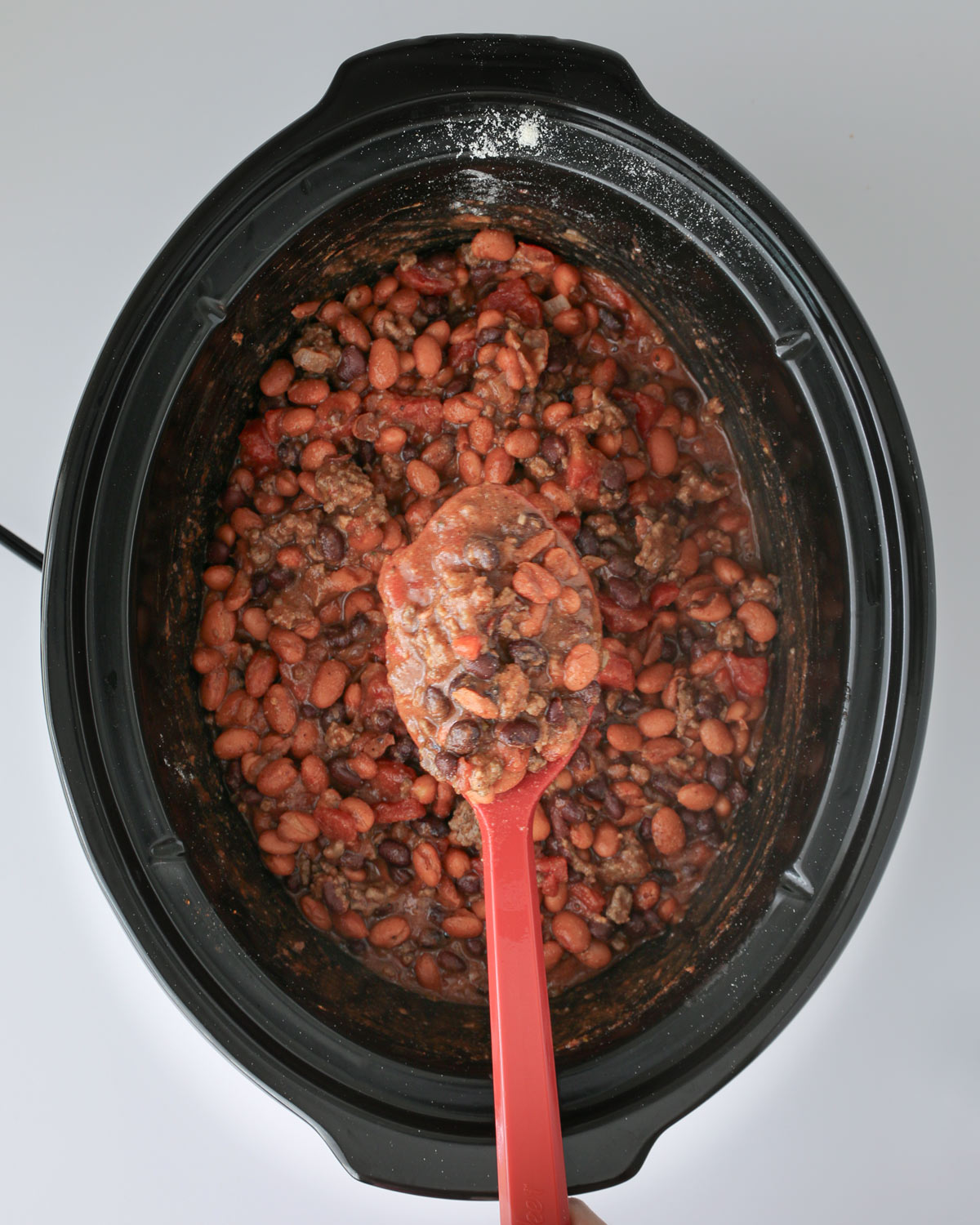 crockpot of chili, with a red spoon holding a big scoop of chili.