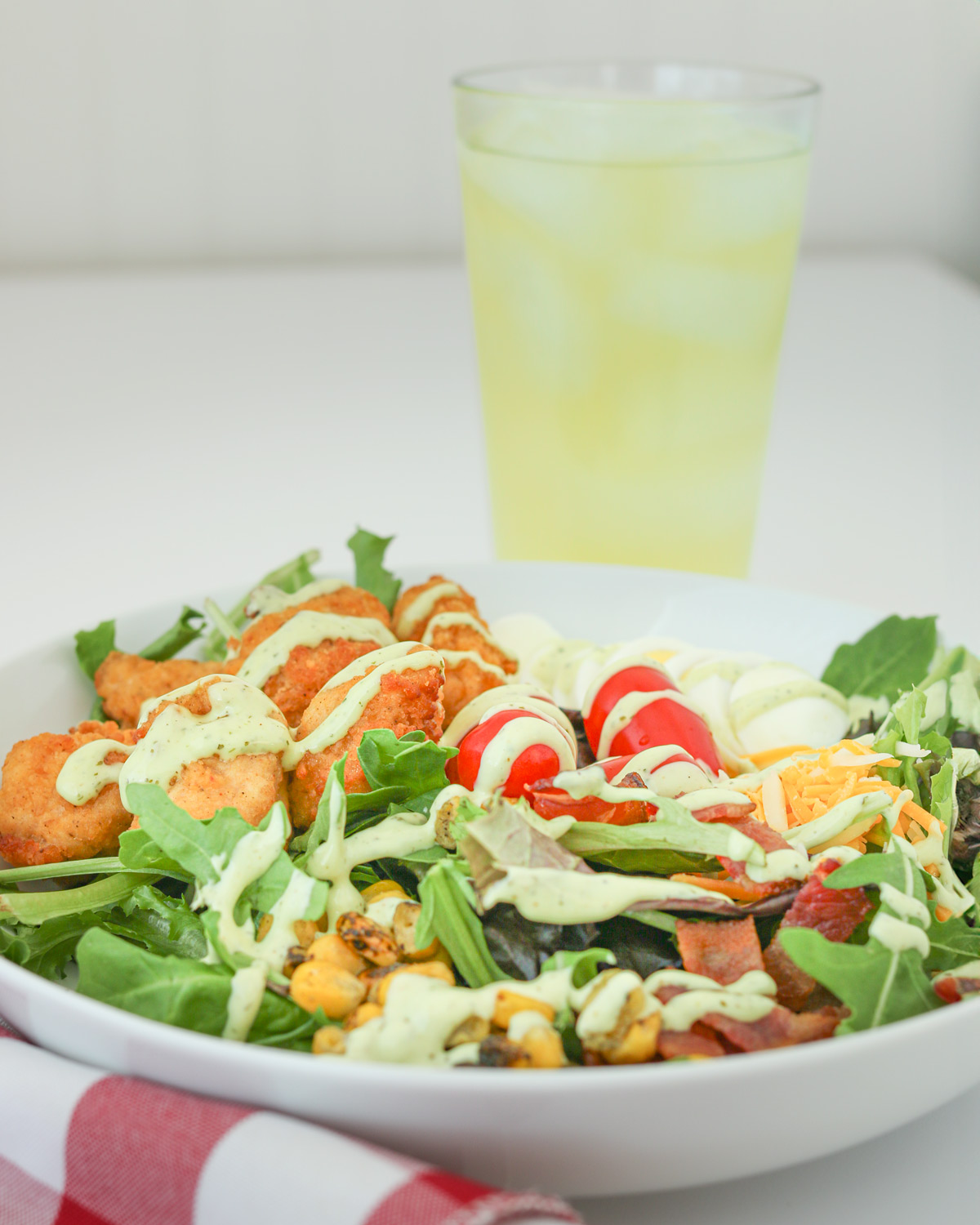 side shot of a chick-fil-a cobb salad with a glass of lemonade in the background.