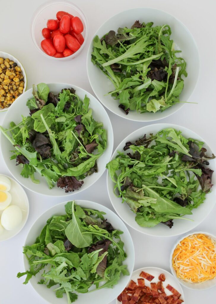 baby greens divided into four bowls with other toppings nearby.