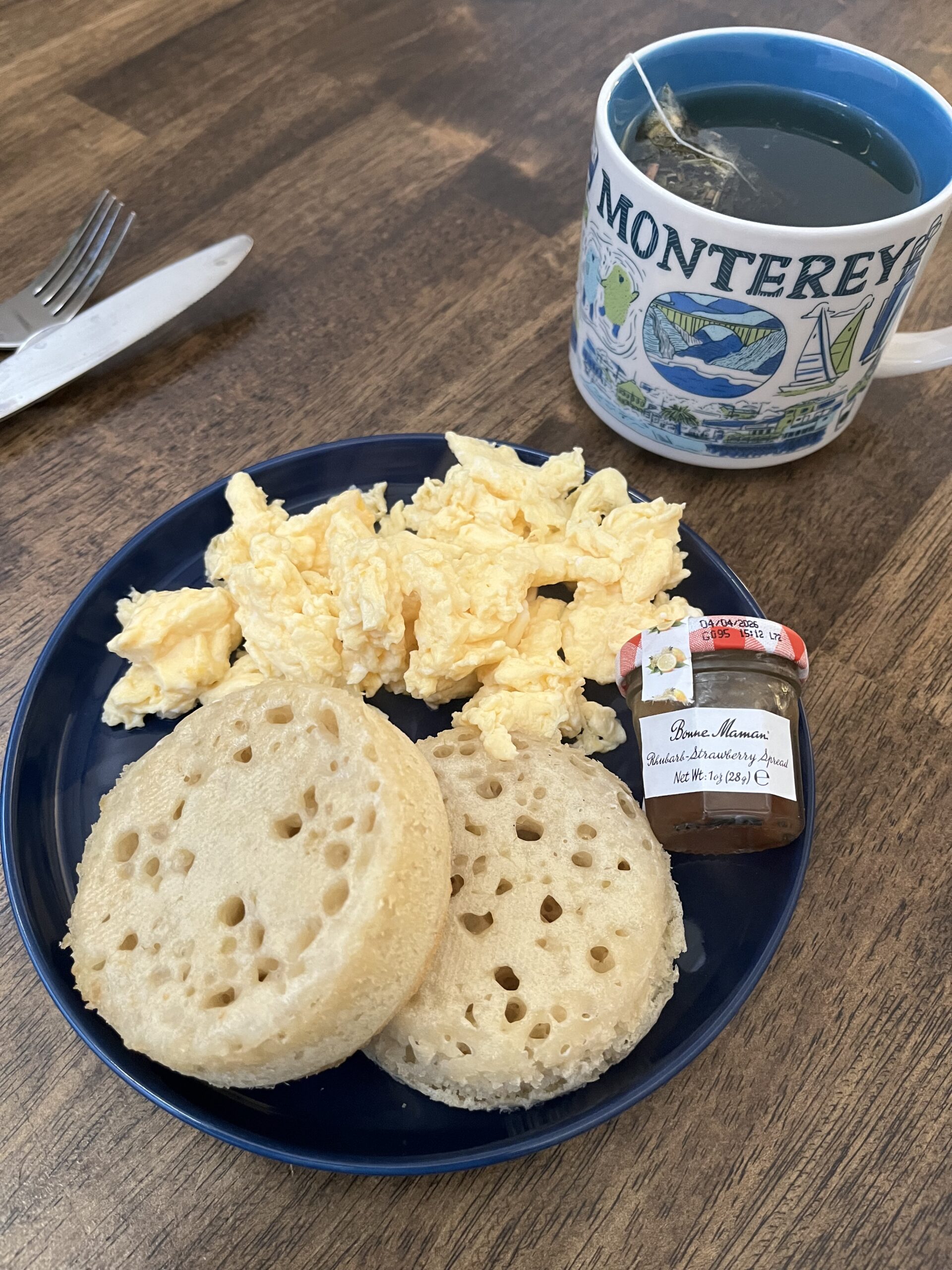 Crumpets and scrambled eggs on blue plate with Monterey mug of tea.