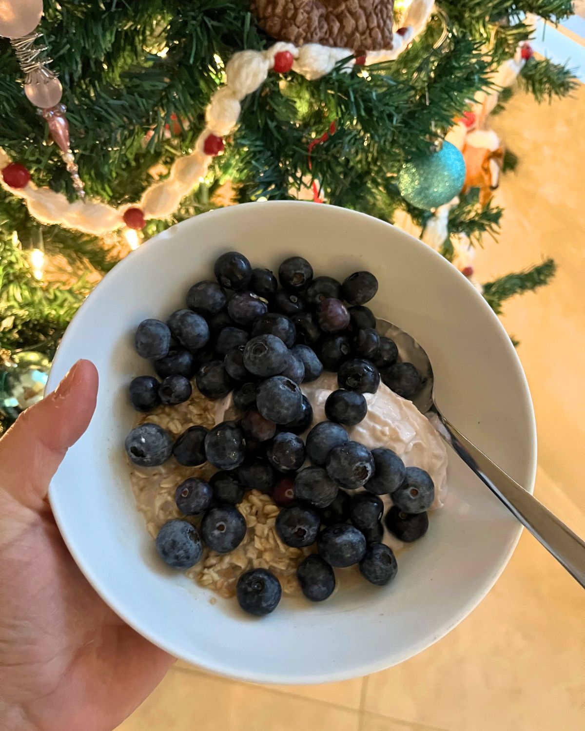 holding breakfast bowl by christmas tree.