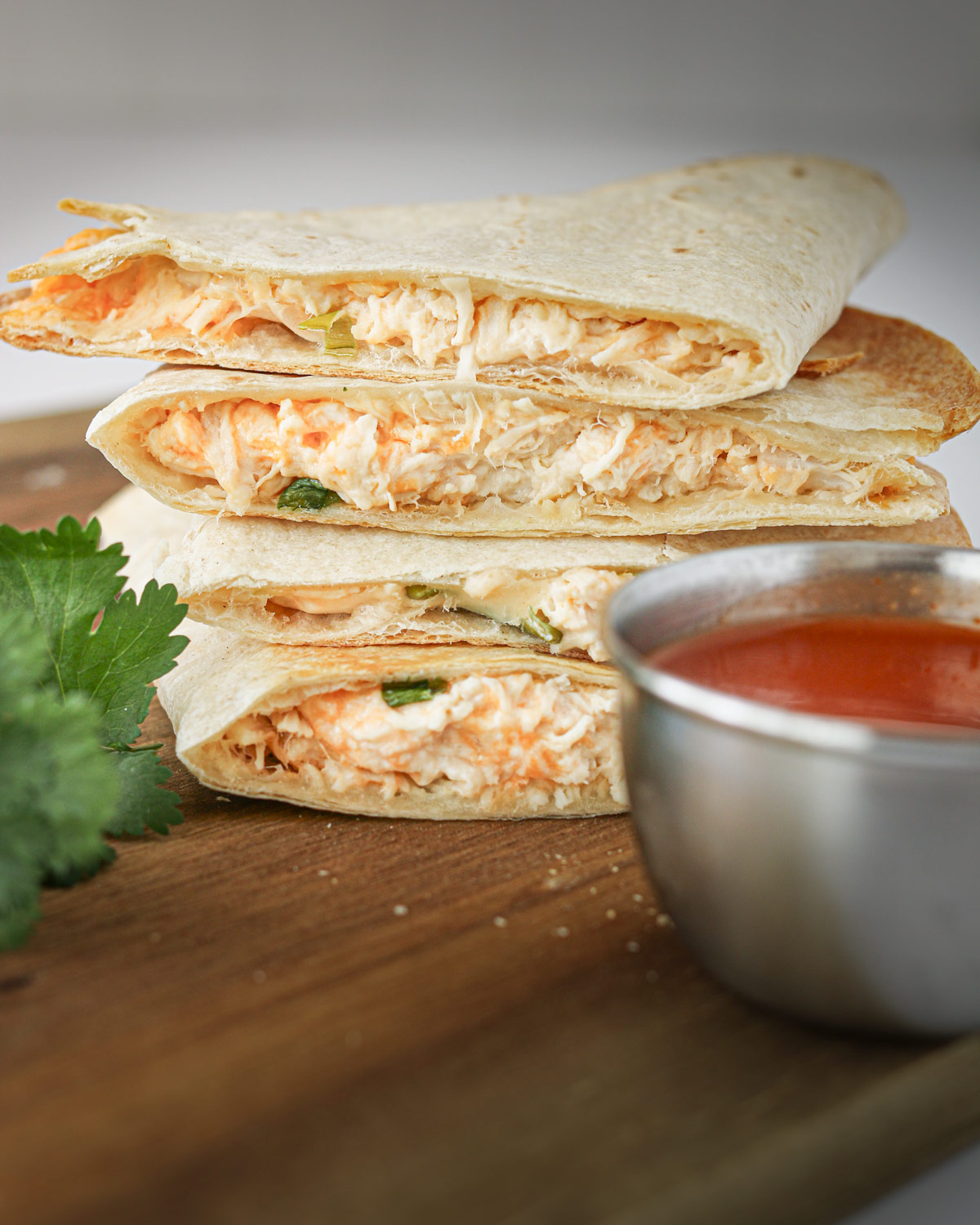 buffalo chicken quesadillas stacked on a wooden board with sauce in a cup.