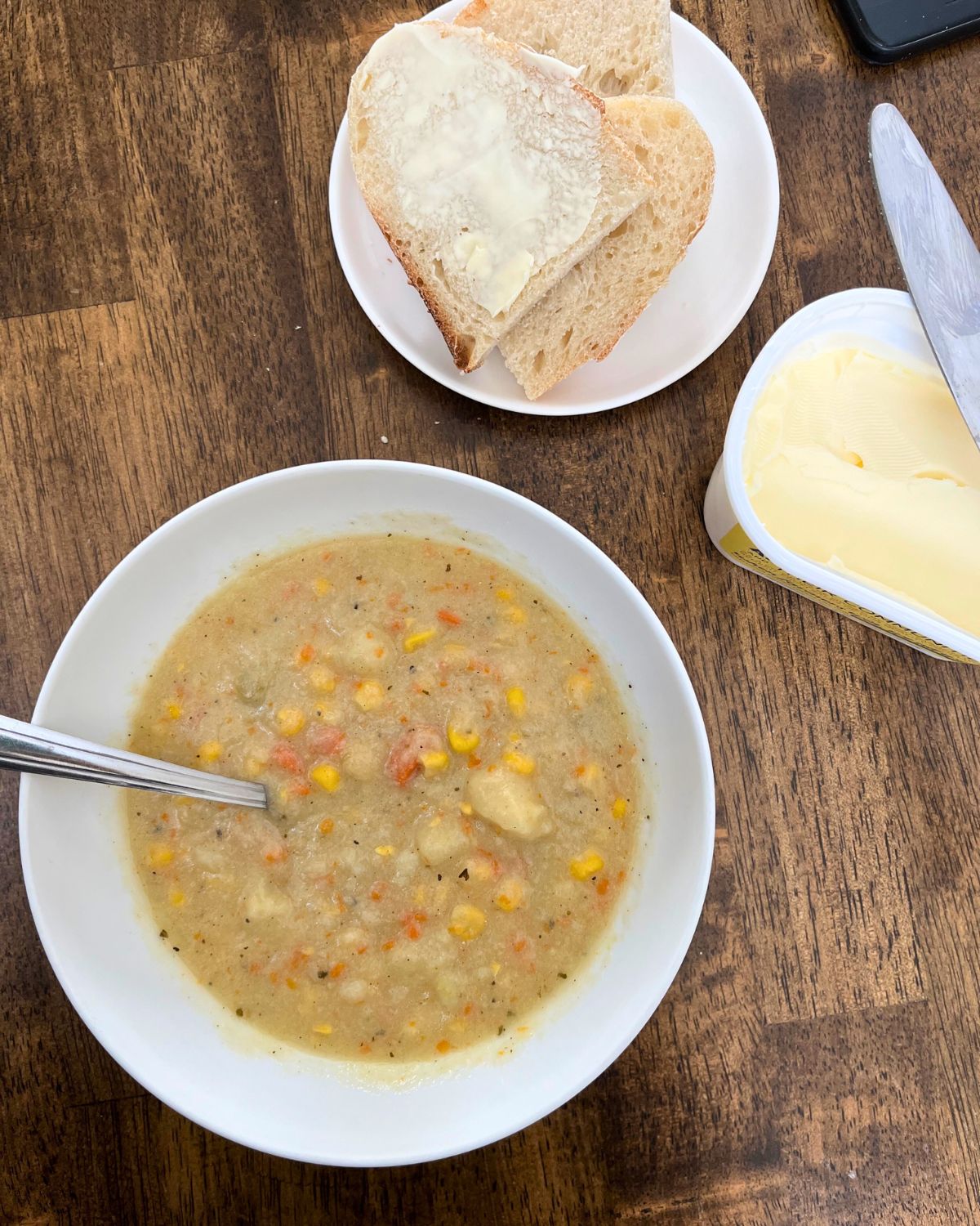 bowl of soup with plate of bread and tub of butter.