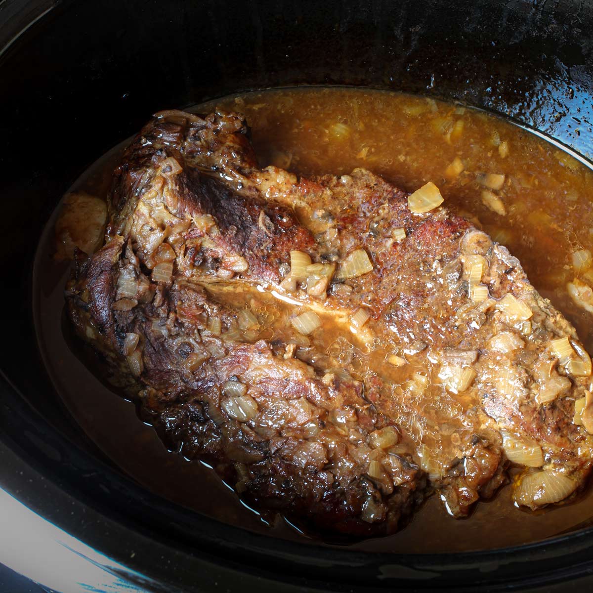 chuck roast in pot with gravy surrounding the meat.