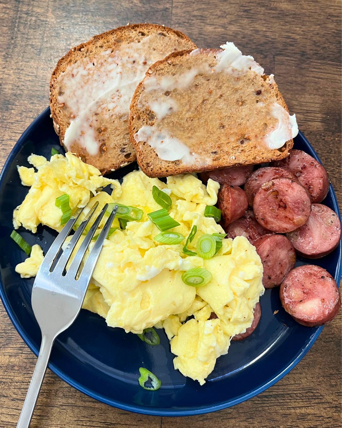 eggs with scallions, sausage, and toast on a plate.