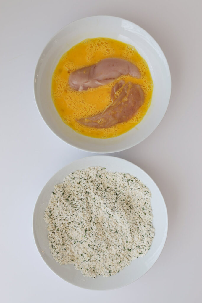 chicken strips in egg mixture with flour mixture in bowl nearby.