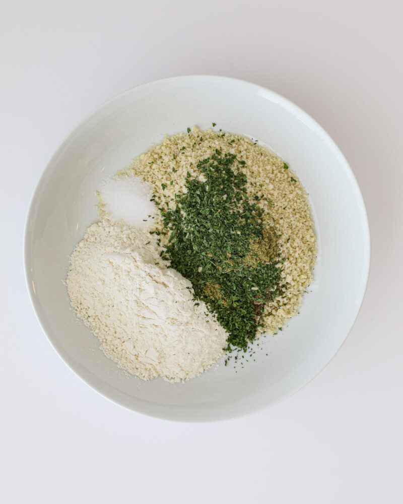 flour, bread crumbs, spices, and herbs in shallow white bowl.