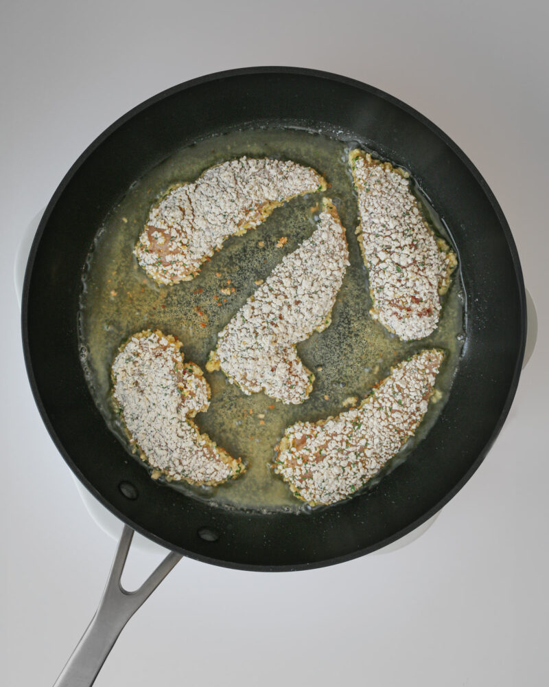 breaded chicken strips in frying pan with oil.