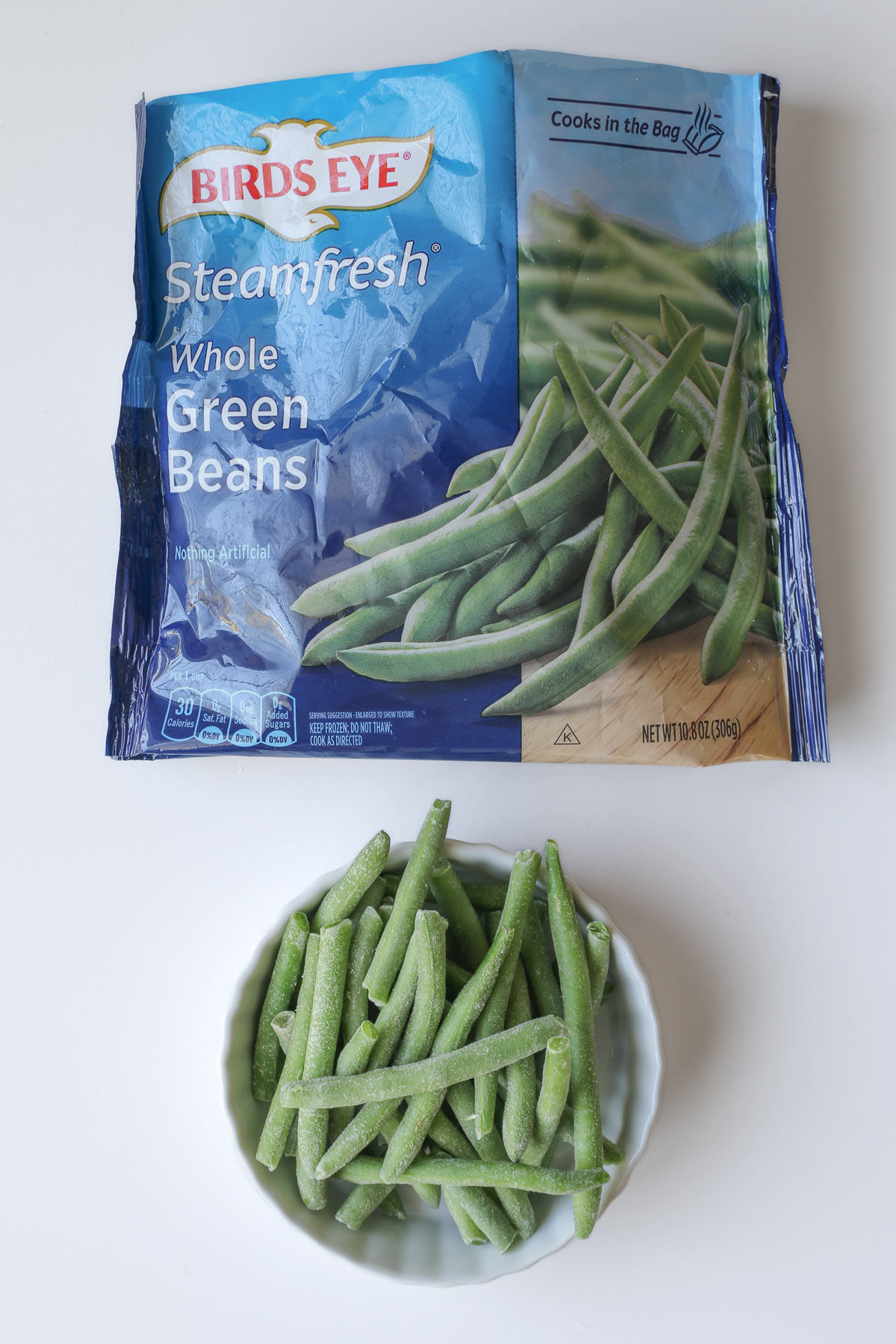 whole green beans in a bowl next to the open bag.