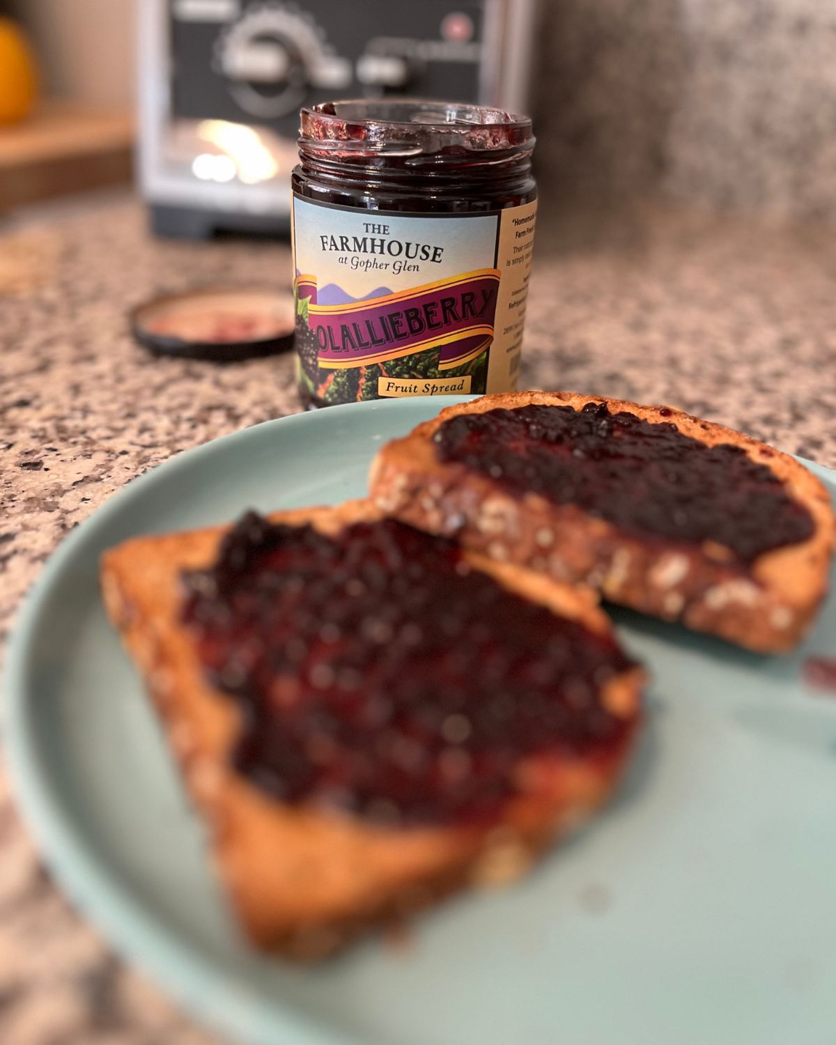 jar of jam next to teal plate holding two slices of toast with jam on them.