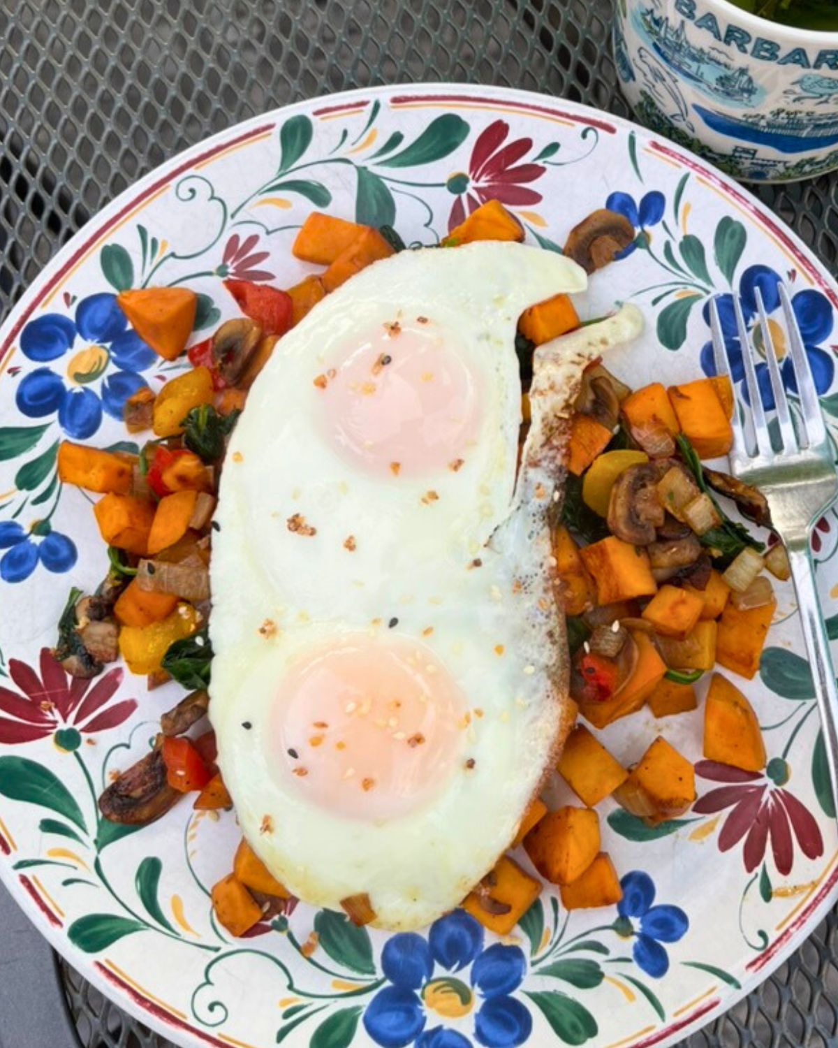 two fried eggs atop a plate of vegetable hash.