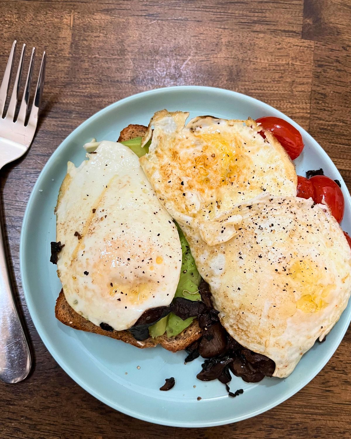 fried eggs on toast on a blue plate with fork and knife.