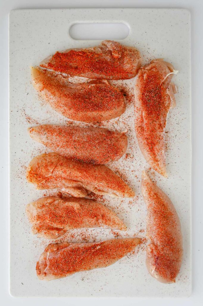 chicken tenders on cutting board seasoned with spices.