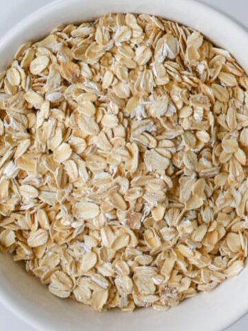 close up of rolled oats in a white bowl on a white counter.