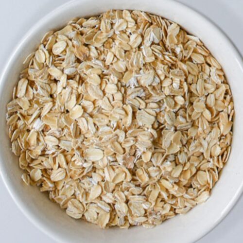 close up of rolled oats in a white bowl on a white counter.