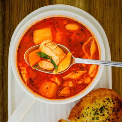 overhead shot of bowl of soup on a tray with garlic bread nearby, a spoon full of soup is resting on the bowl.