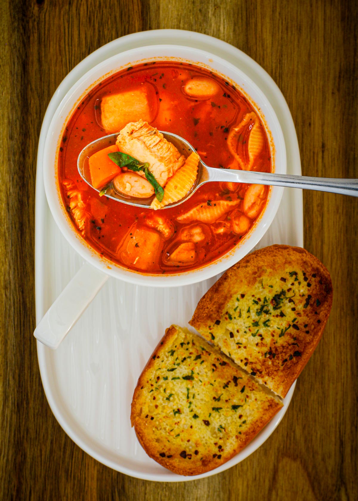 bowl of soup on a white oval tray with pieces of garlic bread nearby.