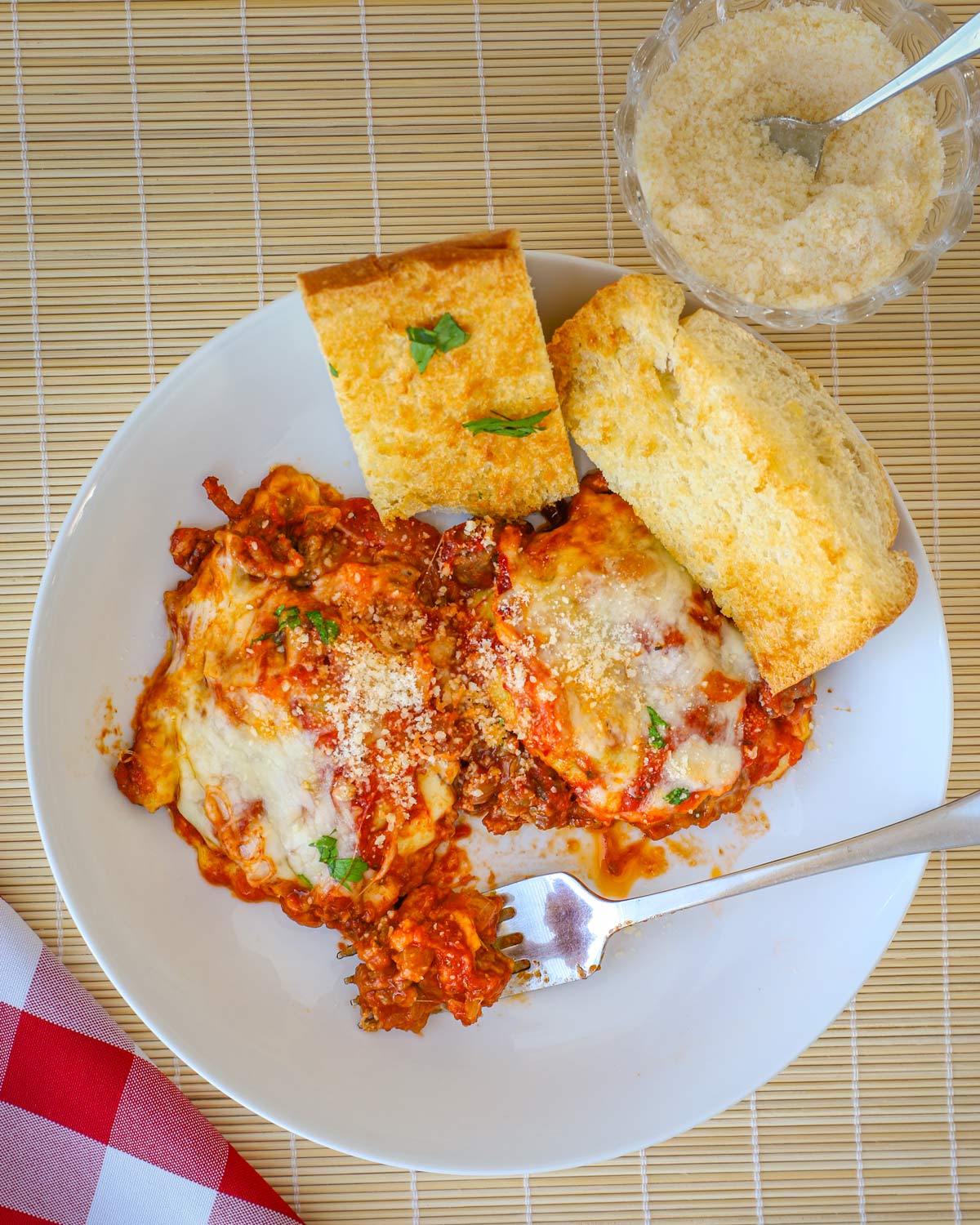 plate of ravioli casserole and garlic bread on set table, with dish of parmesan nearby.