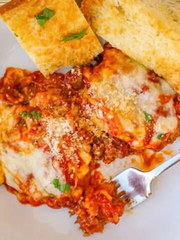 ravioli casserole in white bowl with garlic bread slices.