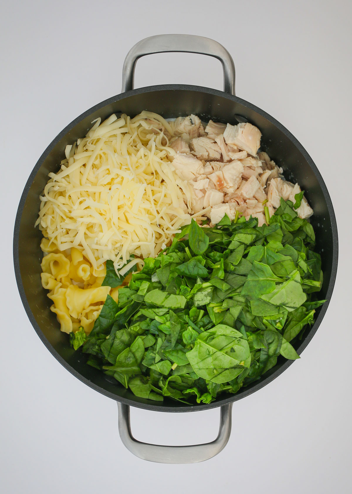adding chicken, cheese, pasta, and spinach to the sauce in the pot.