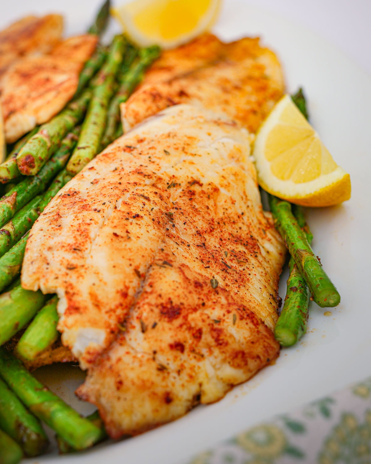 close up of cooked fish on a platter with asparagus and lemon wedges.