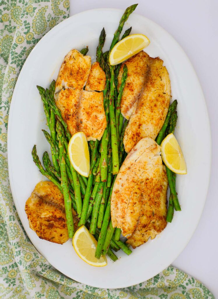 a large platter of fish, asparagus, and lemon wedges.