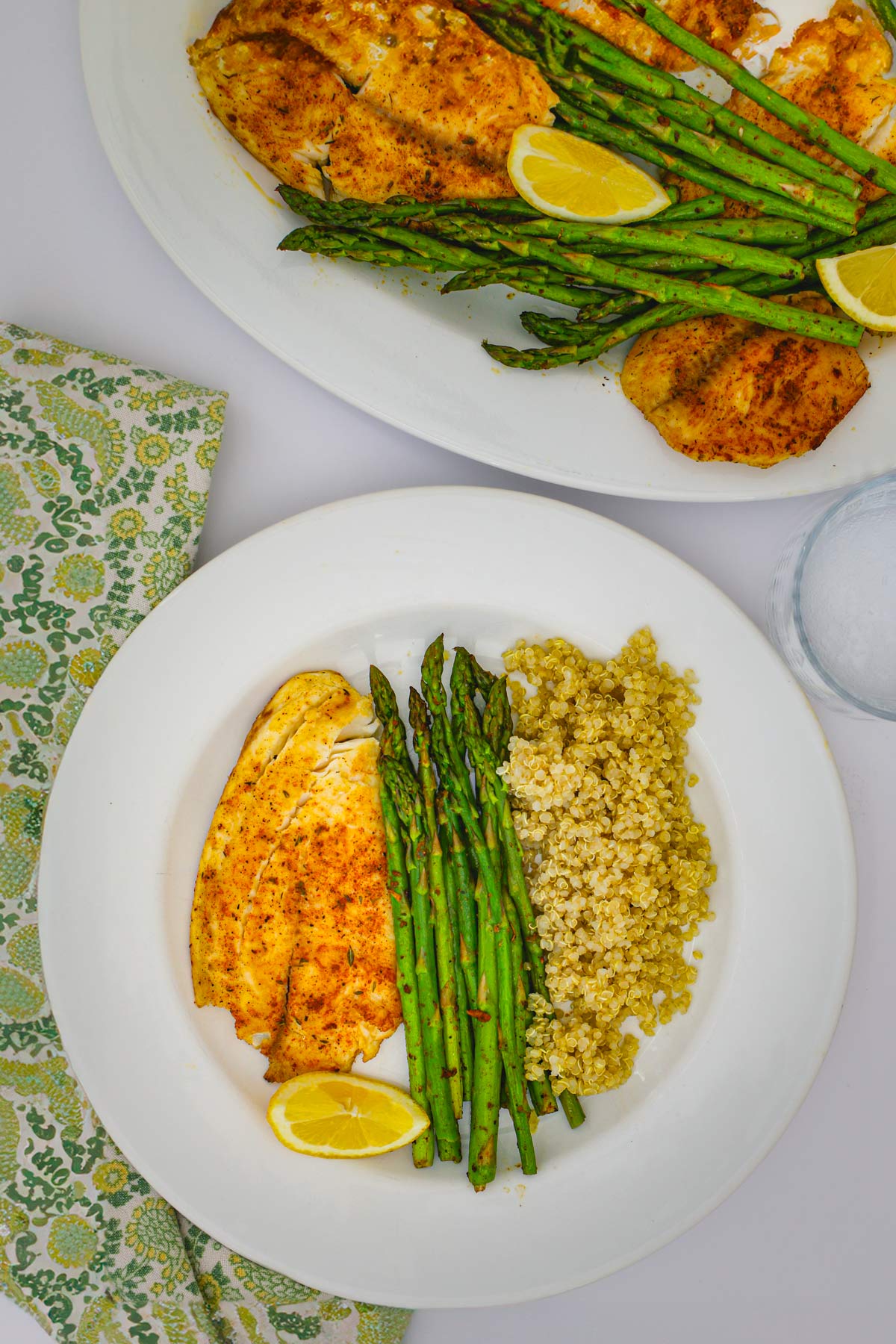 dinner table with platter of fish and a dinner plate filled with fish, asparagus, and quinoa.
