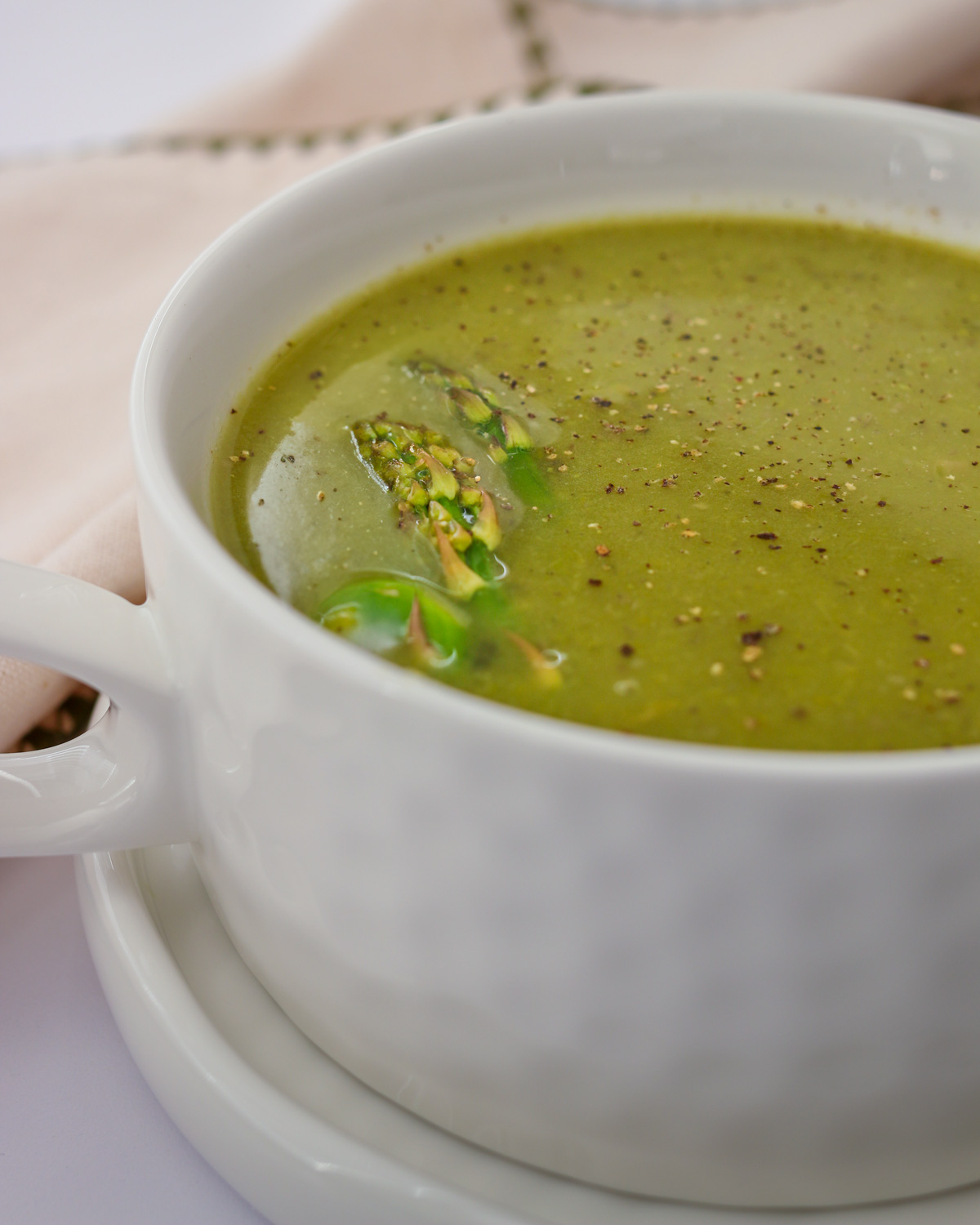 asparagus soup in a white hammered dish, with pepper sprinkled on top.