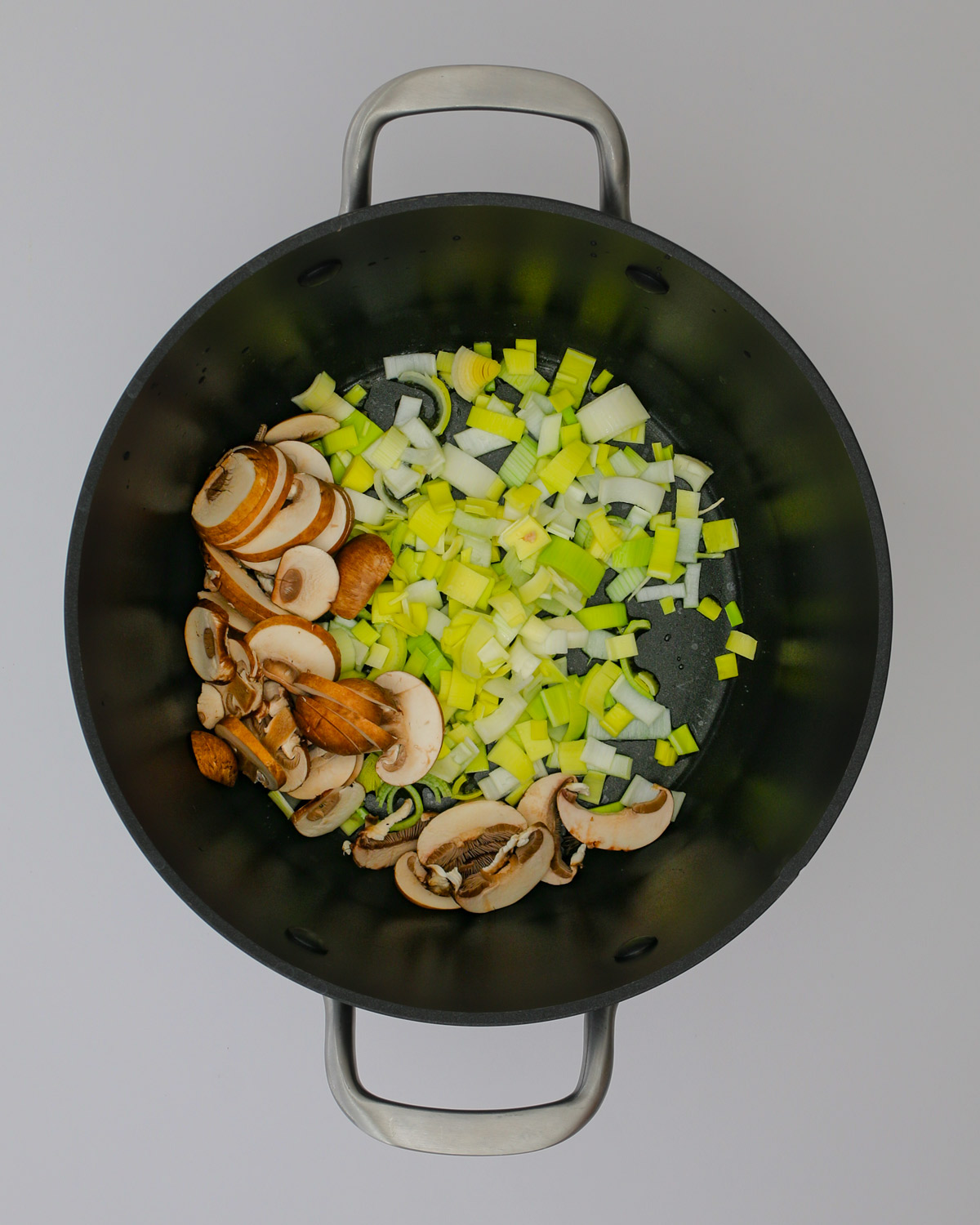 adding mushrooms and leeks to hot oil in the pot.