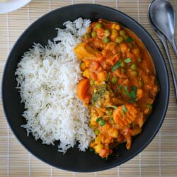 black dish of veggie curry and rice with a spoon to the side.