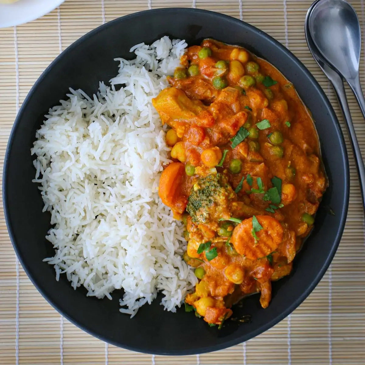 black dish of veggie curry and rice with a spoon to the side.
