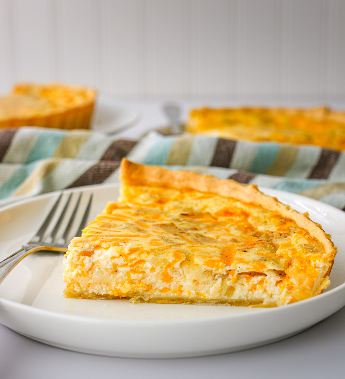 slices of cottage cheese quiche on plates with forks and a striped towel.