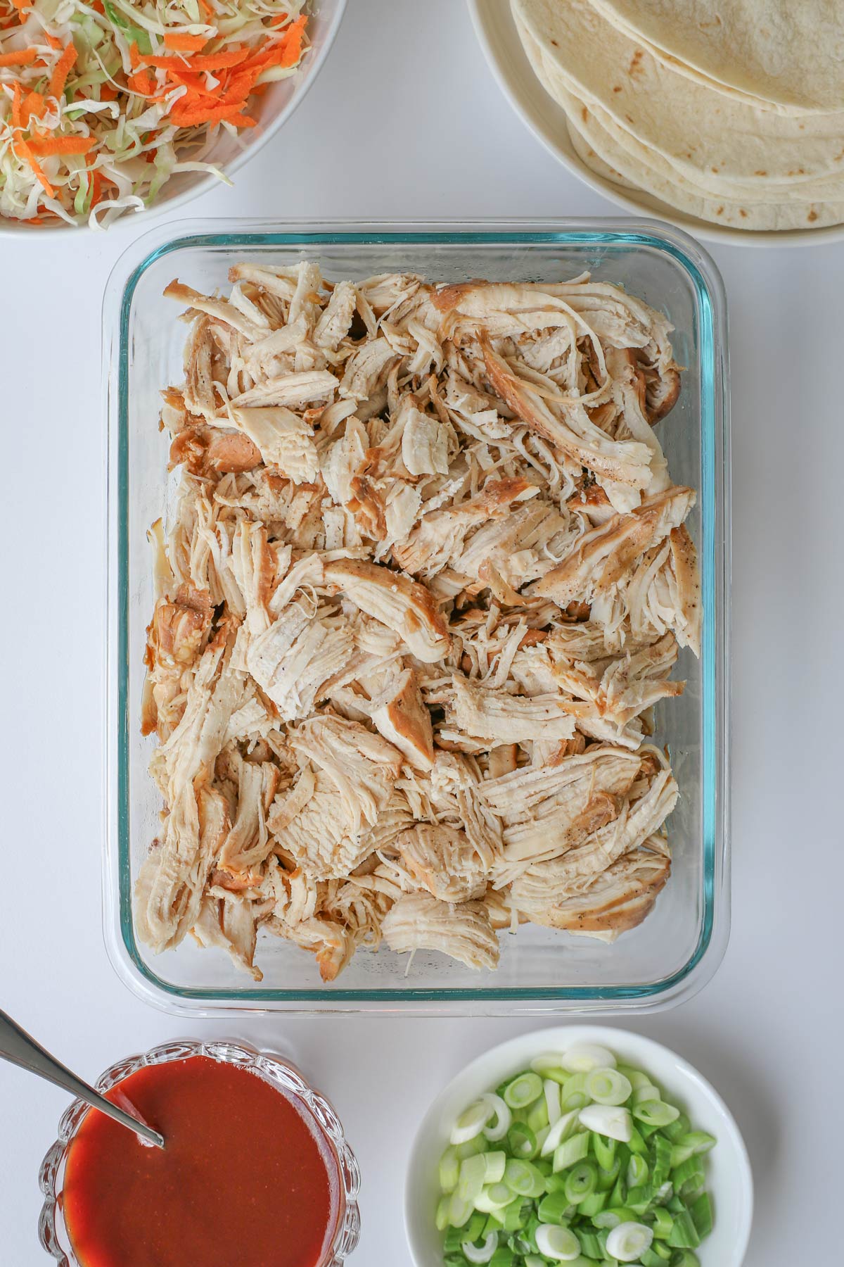 shredded chicken in dish with elements for serving surrounding.